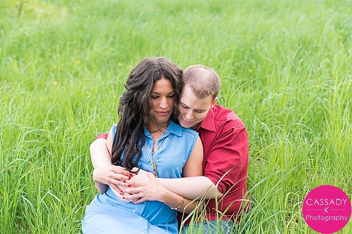 Couple snuggling in lush green grass for a Rockwood Hall Engagement Session in Rockafeller Reserve State Park, New York
