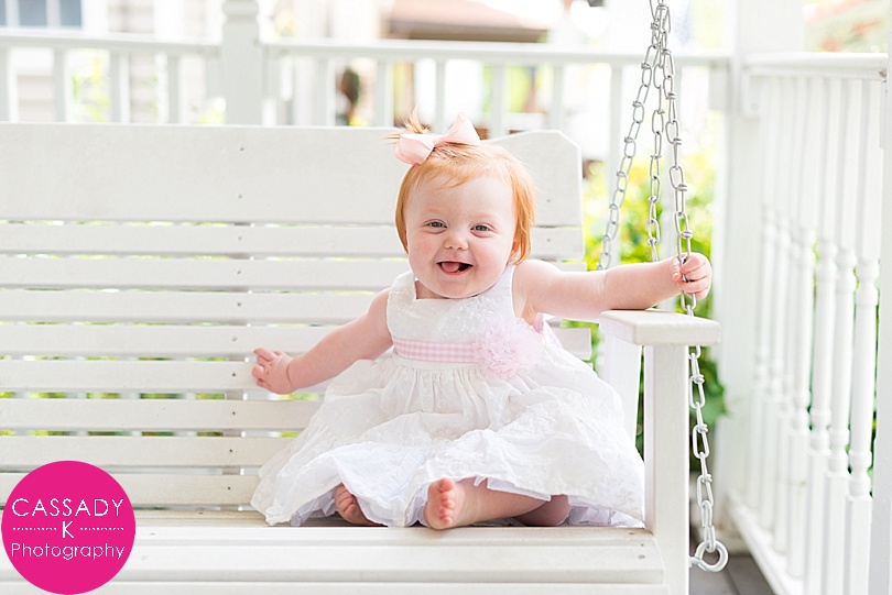Baby girl sitting on white swing for first birthday portraits