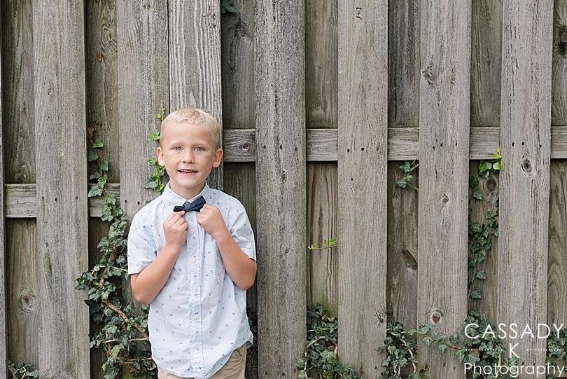 Young boy straightening his tie agains an ivy fence during his 7 year old portraits
