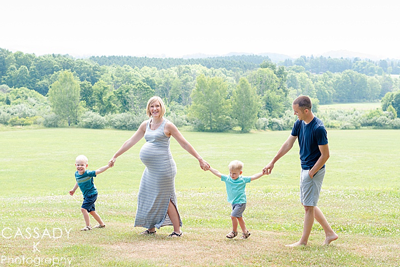 Family walking with a scenic tree line behind them during an outside family maternity session