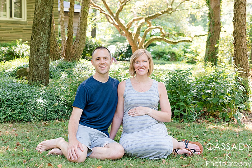 Mom and dad sitting in the grass during the summer awaiting the arrival of their third son during an outside family maternity session by Cassady K Photography