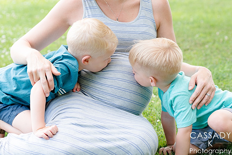 Big brothers kissing their mom's pregnant belly during an outside family maternity session