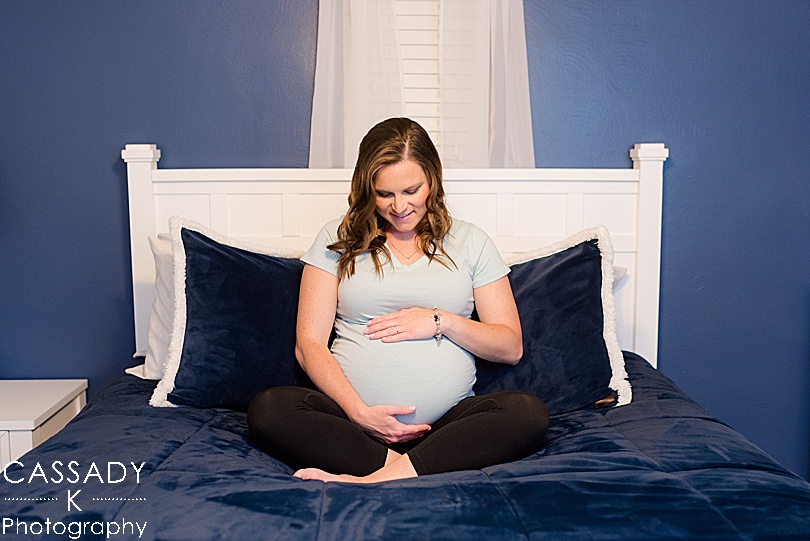 Pregnant mother sits in a blue bed and looks down at her pregnant belly during a Pittsburgh Maternity Session