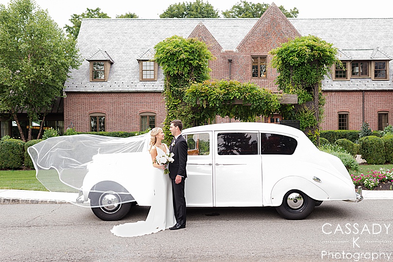 Bride and Groom in front of a white Rolls Royce with her cathedral length veil blowing at a Small Ninety Acres Wedding