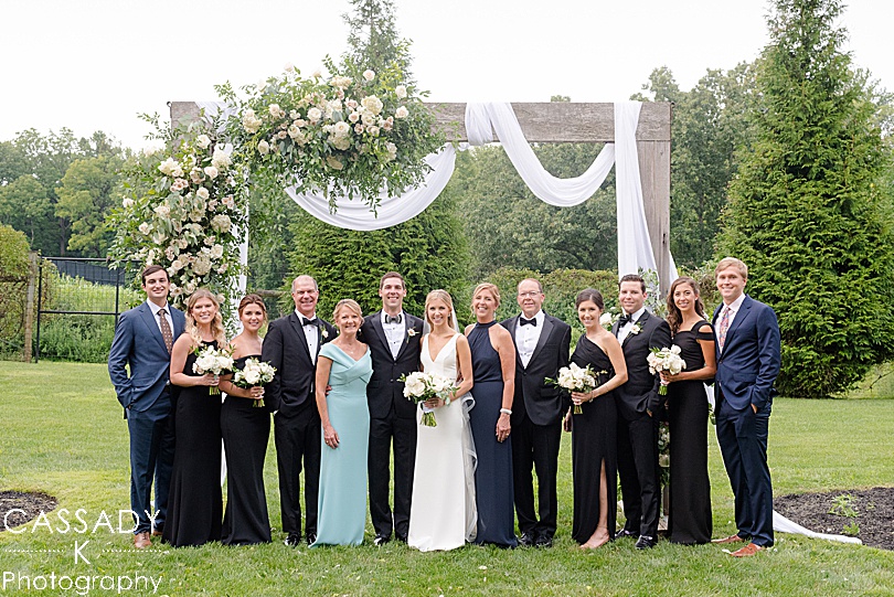 Family portrait in front of floral decorated arbor at a Small Ninety Acres Wedding in Natirar of Peapack, NJ