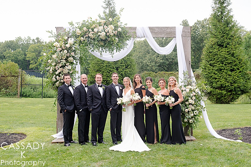 Bridal Party portrait in front of floral decorated arbor at a Small Ninety Acres Wedding in Natirar of Peapack, NJ