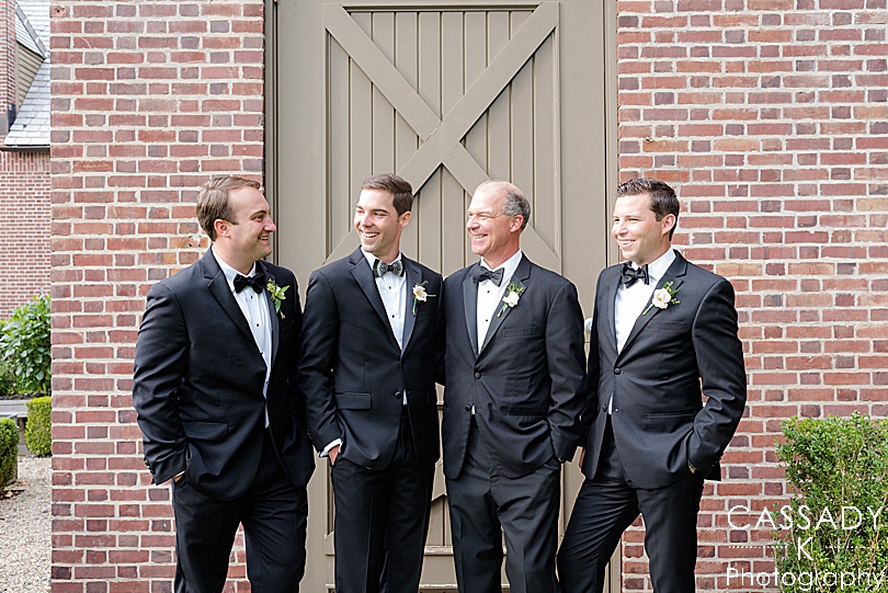 Groomsmen talking to each other in front of barn door during a Small Ninety Acres Wedding in Natirar of Peapack, NJ