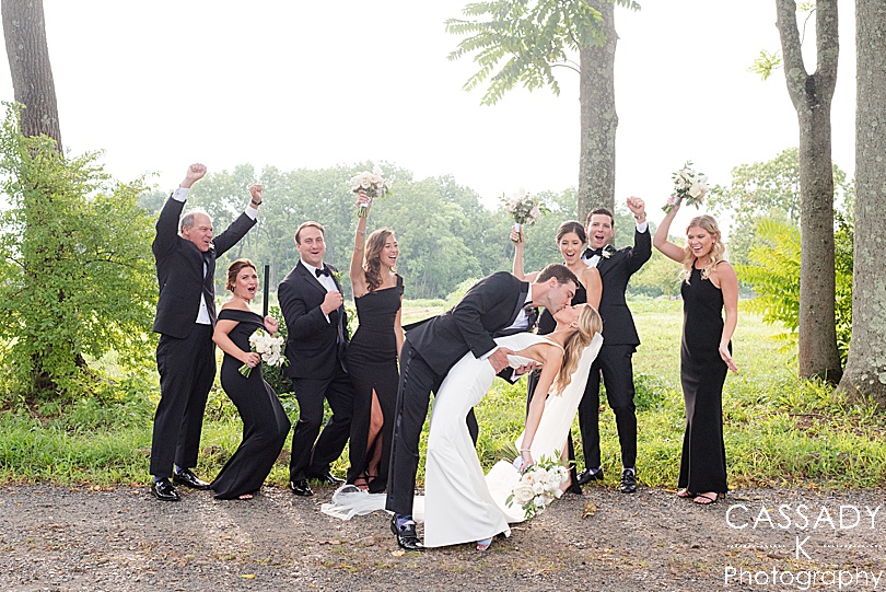 Bride and Groom kiss while bridal party cheer them on during a Small Ninety Acres Wedding in Natirar of Peapack, NJ