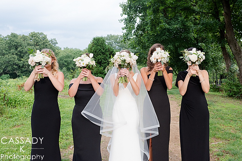 Bride & Bridesmaids hold white bouquets in front of their faces during a Small Ninety Acres Wedding in Natirar of Peapack, NJ