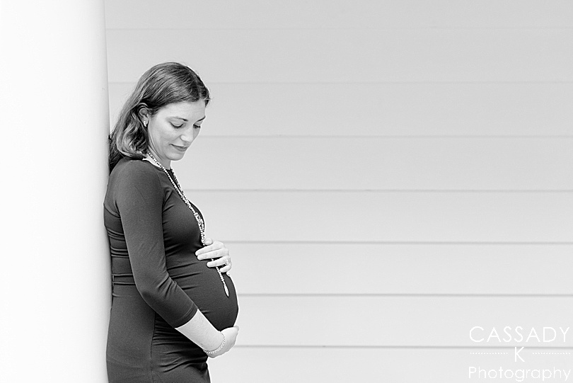 Pregnant woman leans against a column and cradles belly outside during a fall maternity session in Westchester County, NY