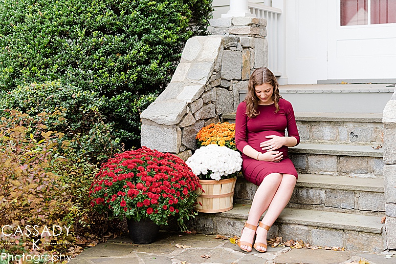 Pregnant mom sits on front steps of home during an outside fall maternity session in Westchester County, NY