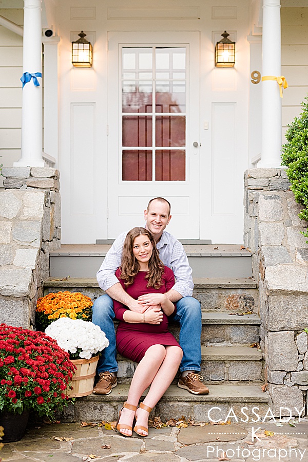 Pregnant wife and husband sit on front steps of home during an outside fall maternity session in Westchester County, NY