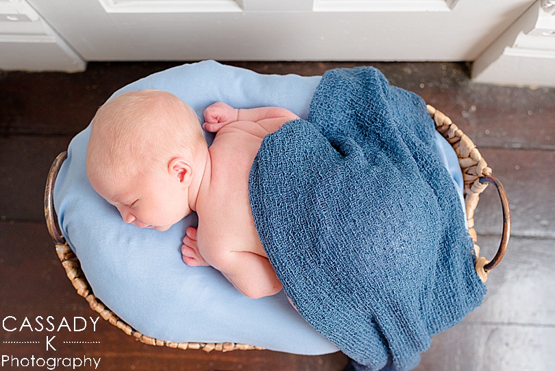 Overhead picture of a baby boy laying in a basket with a blue blanket during an at home Williamsport Newborn Session in PA