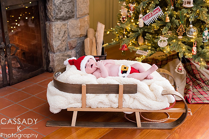 Baby in a Santa newborn outfit, in a sled under the Christmas Tree during an at home Bedford newborn session in NY