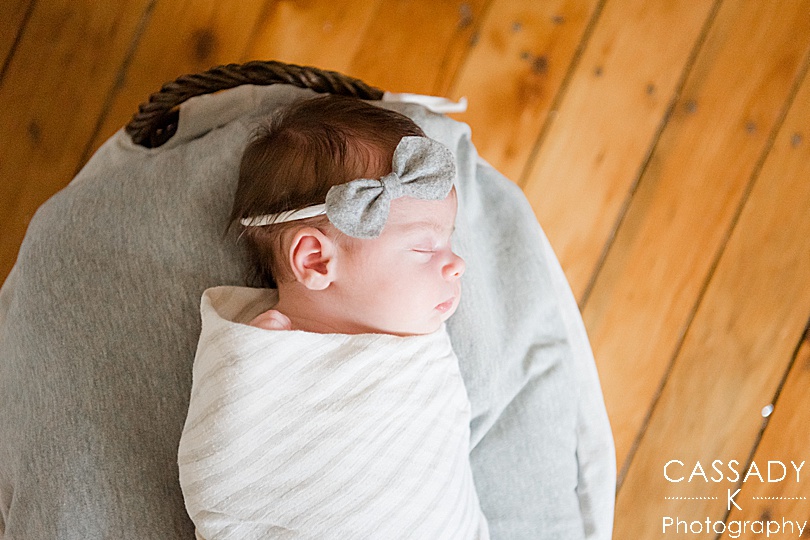 Baby girl in a basket wrapped in a white blanket and wearing a gray headband during an at home Pittsburgh newborn session