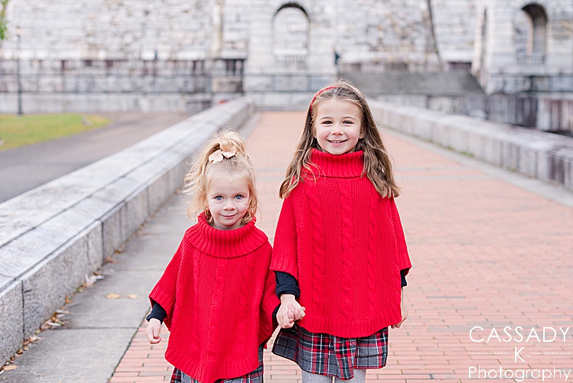 Girls in red ponchos walk down brick path during fall mini sessions in Westchester County, NY for a 2020 photography review