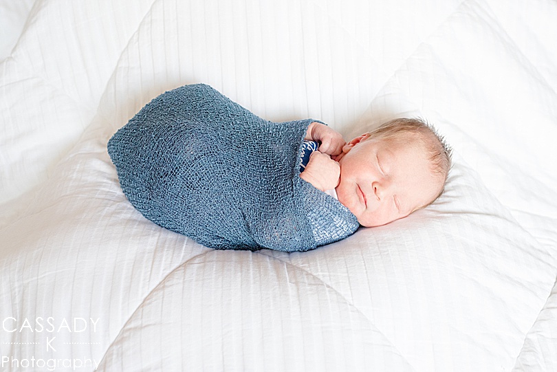 Baby wrapped in a blue swaddle on a white comforter during a newborn session in Pittsburgh, PA for a 2020 photography review