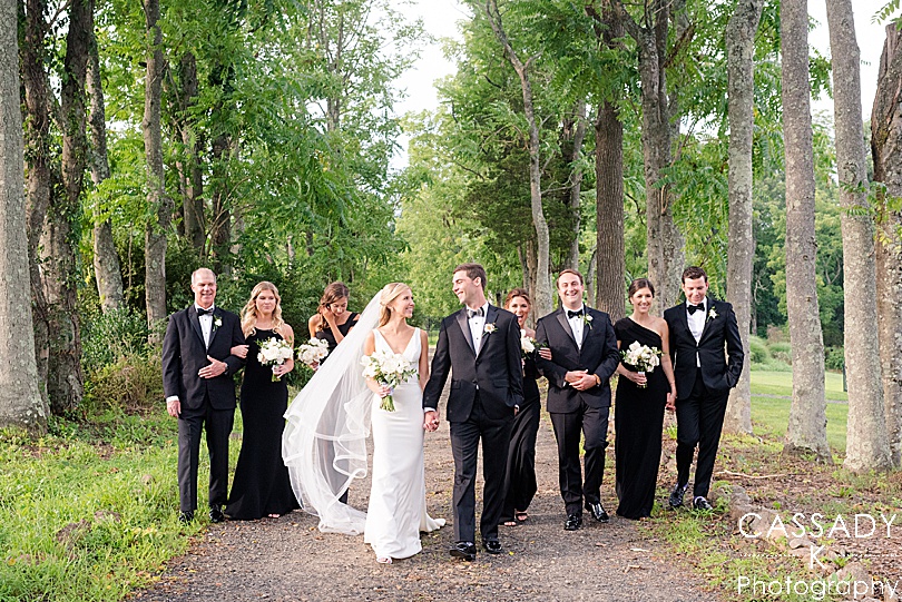 Bridal party walk down between a grove of trees at a small outside Ninety Acres, NJ wedding during a 2020 photography review