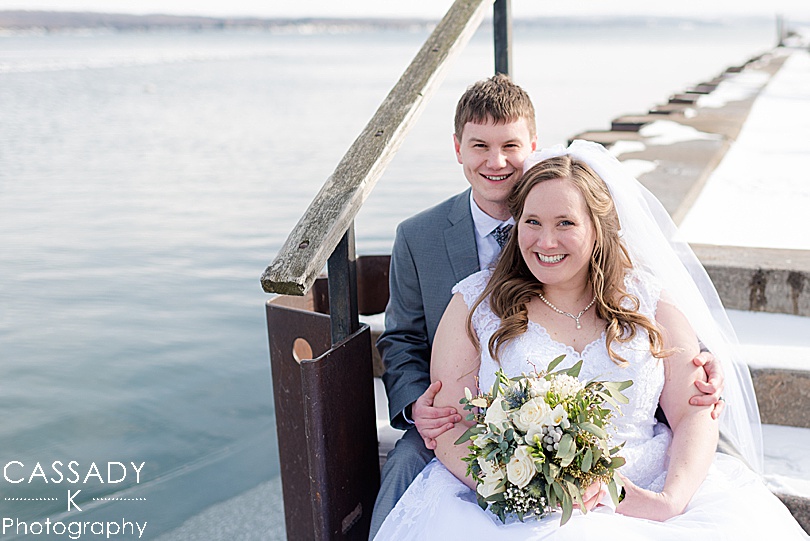 Bride and Groom sit by the lake in the snow on the Canandaigua City Pier for the 2020 photography review