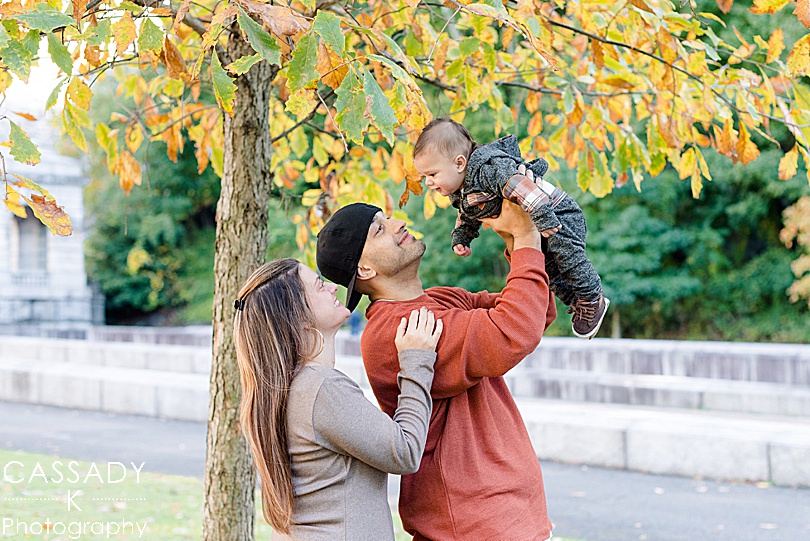 Parents hold up baby under a changing tree during fall mini sessions in Westchester County, NY for a 2020 photography review