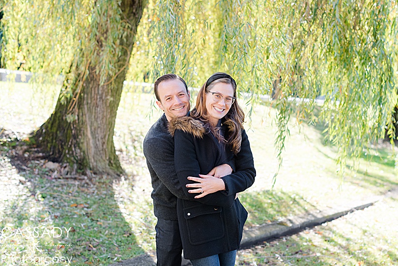Parents cuddle under a willow tree during fall mini sessions in Westchester County, NY for a 2020 photography review