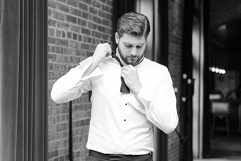 Black and White of Groom tying black bowtie at Ninety Acres while he got ready for a Mansion at Natirar Wedding in Peakpack