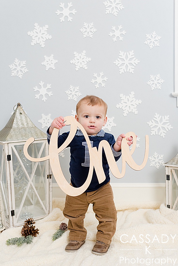Boy holds a die-cut wooden One sign during his Winter Onederland, at home first birthday pictures in Bedford, NY