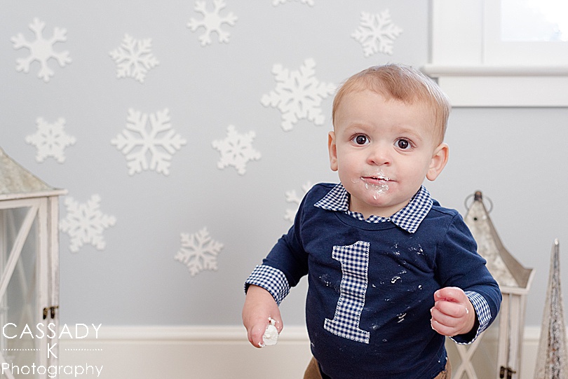 One year old boy has icing on his face from cake smash during his at home first birthday pictures in his Winter Onederland