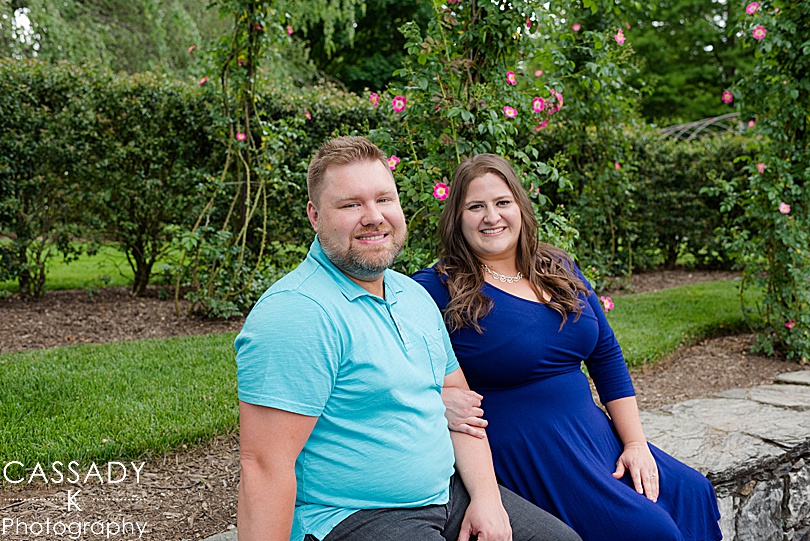Fiances sitting on rock wall in front of roses at Longwood Gardens Engagement Photos