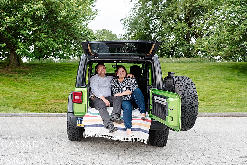 Future bride and groom sit in the back of their bright green Jeep in Kennett Square during engagement photos