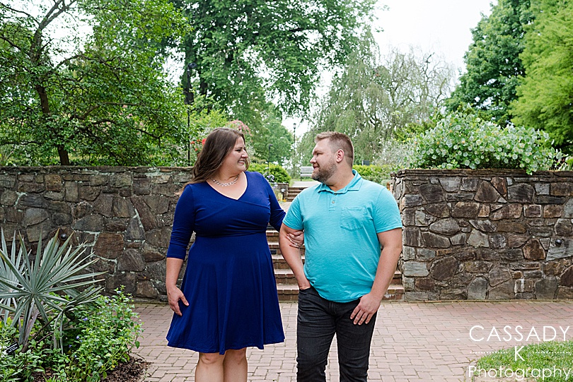 Engaged couple smiling at each other in lush greenery at Longwood Gardens for Engagement Photos