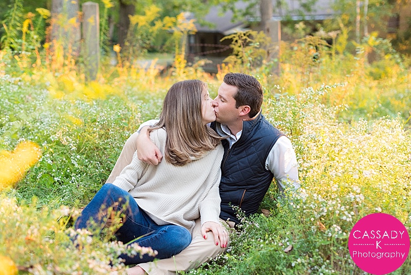 Engaged couple sitting in a field kissing at sunset for a New Jersey Botanical Garden Engagement Session