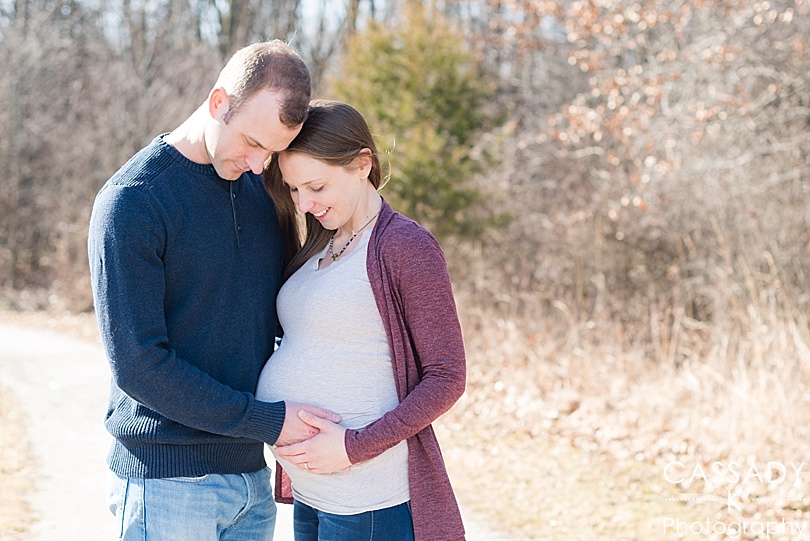 Mom and Dad look at mother's pregnant belly in outdoor winter Family Maternity Session