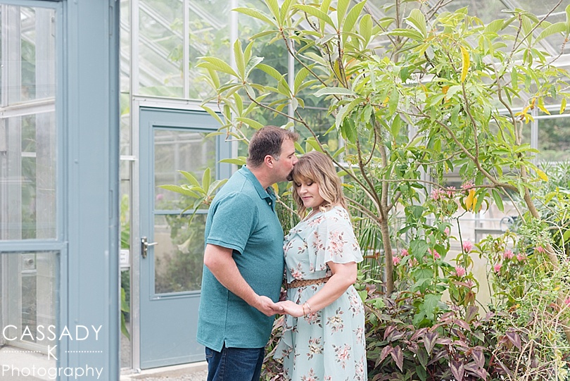 Groom kissing Brides forehead in a greenhouse at a Stonecrop Gardens Engagement Session in Cold Spring, NY