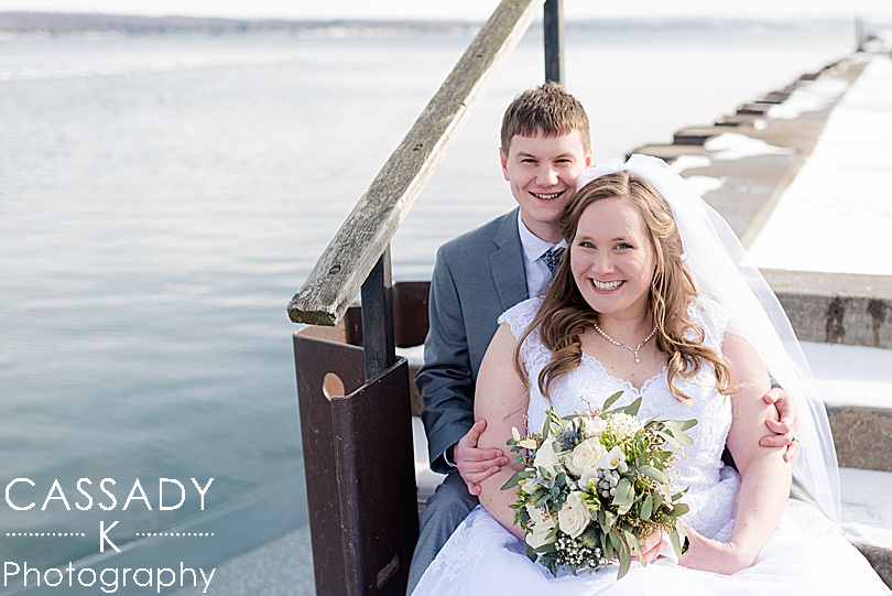 Bride and Groom sitting on the stairs by the water for a winter Finger Lakes Wedding in Canandaigua, NY