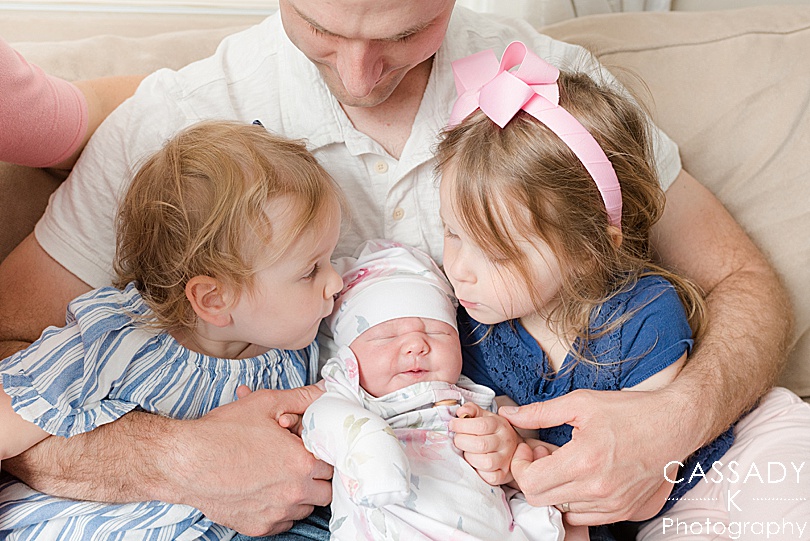 Big sisters kiss their new little sister during a PA Family Newborn Session at home in Lansdale