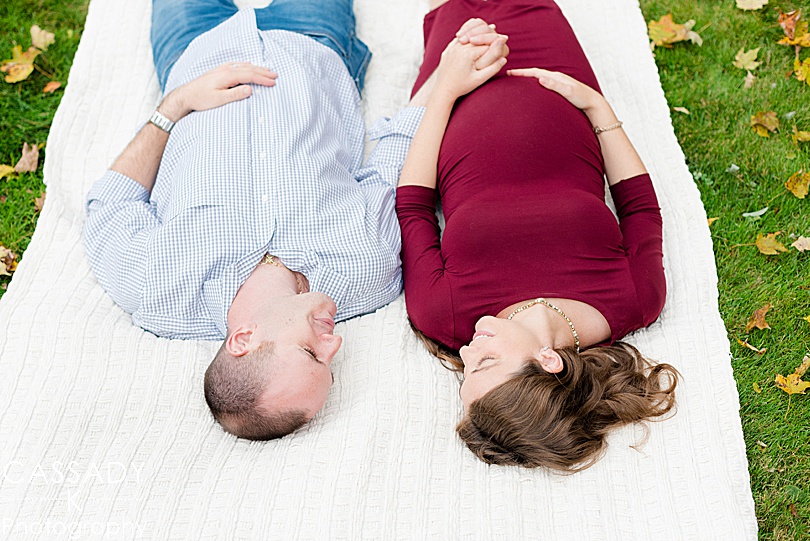 Momma-to-be and husband lie on a blanket during an outdoor fall maternity session in Westchester County, NY