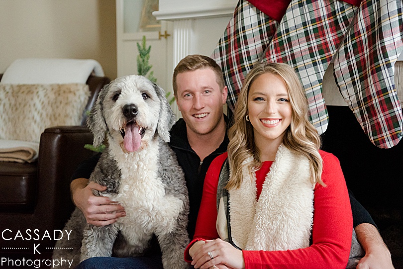 Couple with a Bernidoodle takes Christmas picture in front of the fireplace with stockings for a 2020 photography review
