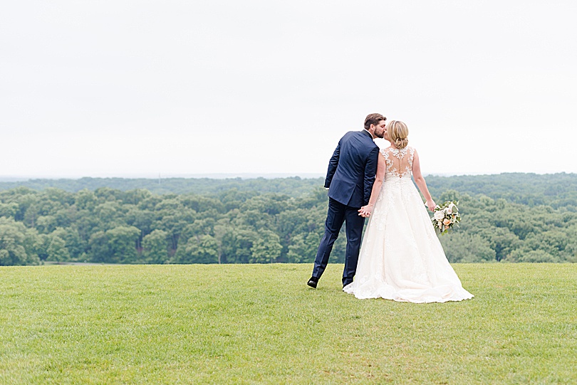 Bride and Groom kiss in grass overlooking a view of the Raritan River and Somerset County for a Mansion at Natirar Wedding