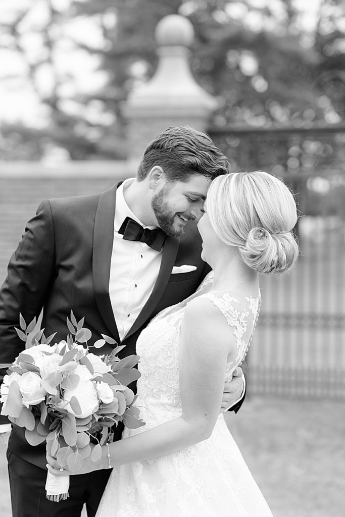 Black and white picture of a Bride and Groom snuggling in front of a wrought iron gate during a Mansion at Natirar Wedding