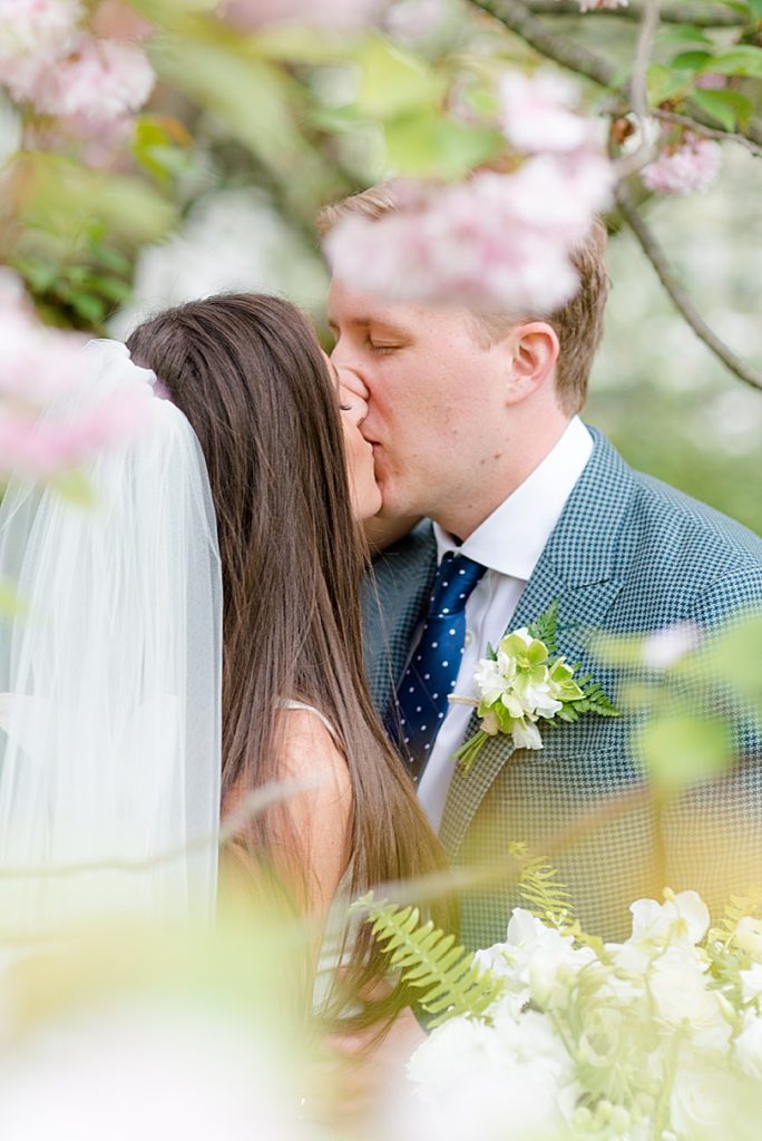 Bride and Groom kiss under the cherry blossoms at Trinity Episcopal Church in Southport, CT during the Tokeneke Club Wedding
