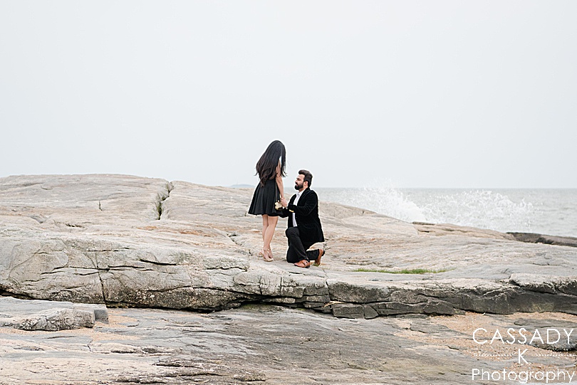 Groom proposes by the water with the waves crashing in the background during a Madison Beach engagement proposal