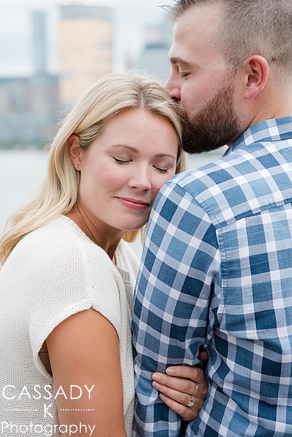 Couple snuggling with NYC skyline behind them during their Jersey City Engagement Session in NJ