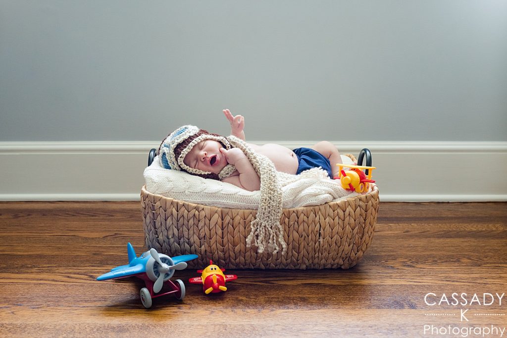 Newborn baby boy in basket with crocheted aviator pilot hat and scarf in Westchester County New York