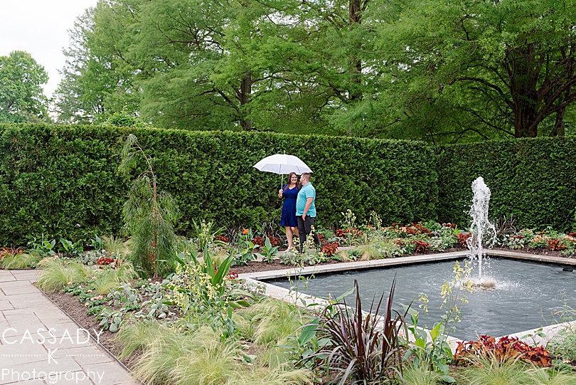 Engaged couple walking in garden with a white umbrella at Longwood Gardens during engagement photos