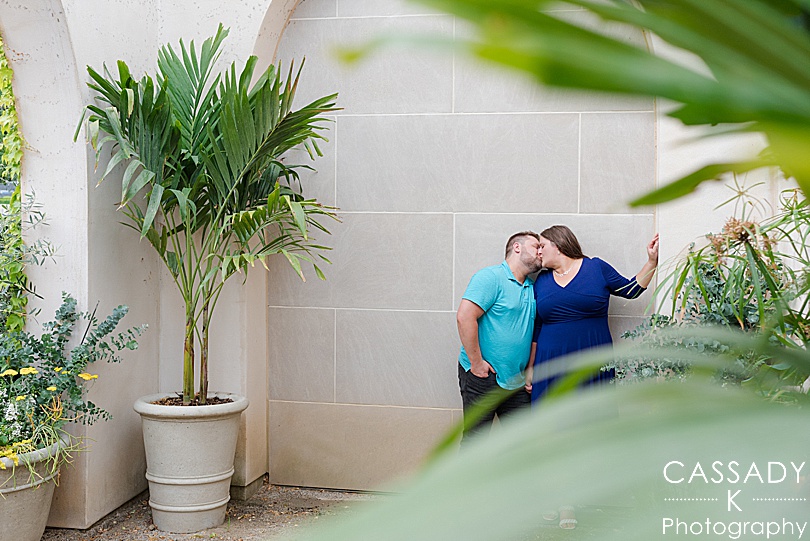 Engaged couple kisses under architecture arch among the lush greenery during Longwood Gardens engagement photos