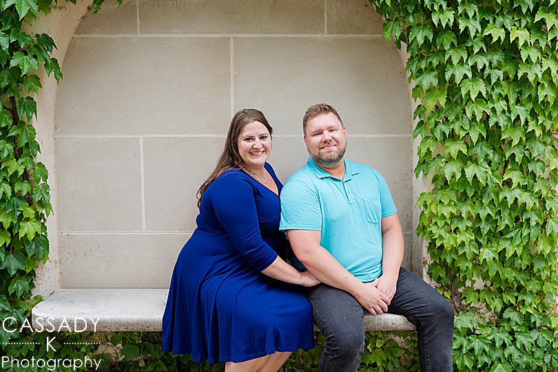 Engaged couple sitting on bench under arch of greenery at Longwood Gardens
