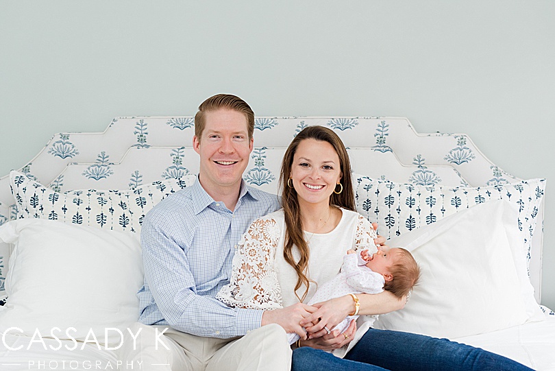 Mom and Dad holding their baby girl on their white and blue bed in Doylestown, PA.