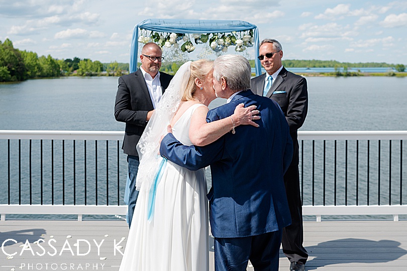 Father kissing bride before getting married along the water