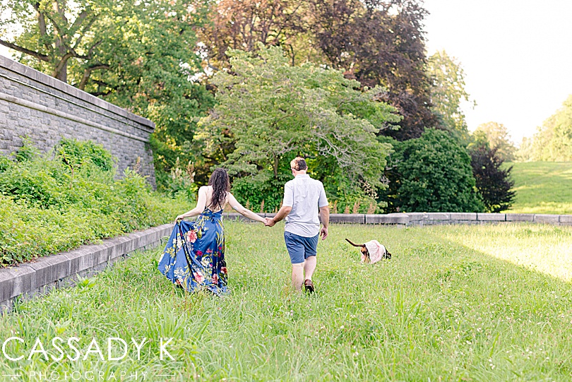 Man and woman walking in field with dog during engagement session